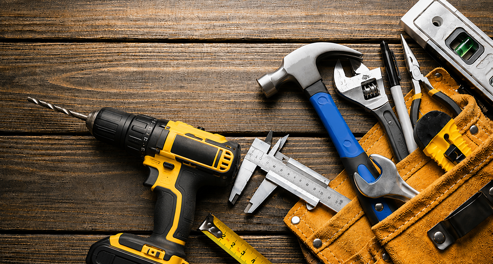 Handyman tools including drill, hammer and tool belt laid out on timber